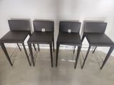 four brown leather bar stools in a row against a white wall