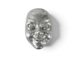 un masque métallique sur lequel est représenté un visage, posé sur une surface blanche