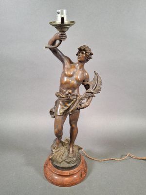 une statue antique en bronze représentant un homme tenant une lampe, posée sur un socle en bois