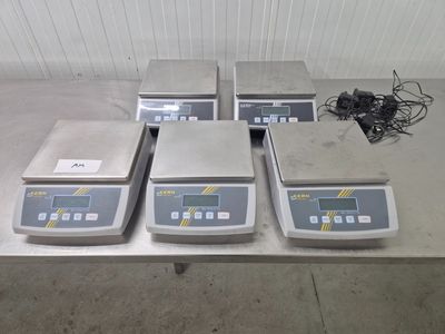 quatre balances électroniques posées sur une table dans un entrepôt