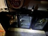 une porte vitrée ouverte laissant entrevoir un réfrigérateur à boissons