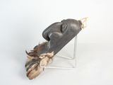 a wooden mask with feathers on a stand on a white surface