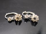 une paire de boucles d'oreilles en argent posées sur une surface noire, sur fond noir