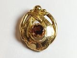 une image représentant une broche de couleur dorée ornée d'un grenat au centre