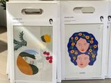 two boxes with paintings on them sitting on a table next to a potted plant