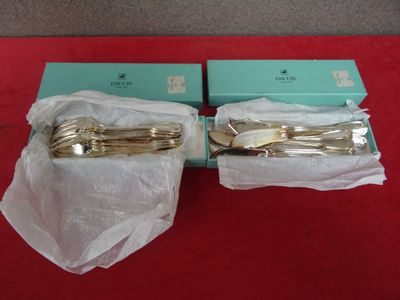 une paire d'ustensiles de service plaqués or, présentés dans leurs boîtes sur un fond rouge