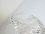 un vase en verre transparent muni d'une anse, posé sur une surface blanche
