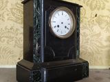 une horloge noire posée par terre devant un mur