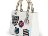 the small white bag has patches on it and a gold handle