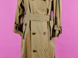 un trench-coat marron posé sur un mannequin, devant un fond rose