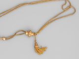 a close up of a gold necklace with a tassel on a chain