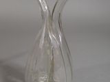 a clear glass vase with a curved handle on a table