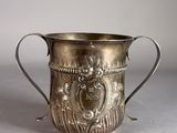 an old silver cup sitting on top of a table next to a white wall