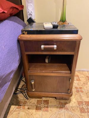 a nightstand with a phone on top of it next to a bed