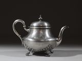 une théière ancienne en argent posée sur un socle, sur fond noir