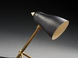 une lampe noire et dorée posée sur un trépied, devant un fond noir