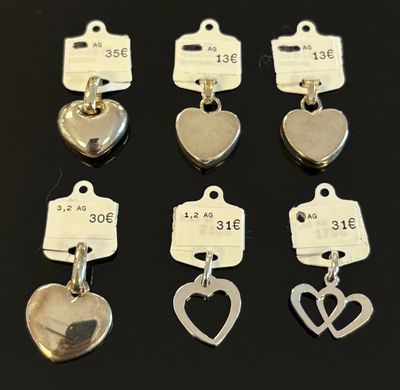 six breloques en forme de cœur en argent, accompagnées de leurs étiquettes de prix, posées sur une table