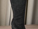 black high heeled boots on a wooden table with curtains in the background