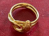 une bague en or ornée d'un nœud, posée sur un fond rouge