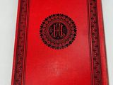a red book with a black border and a monogram on it