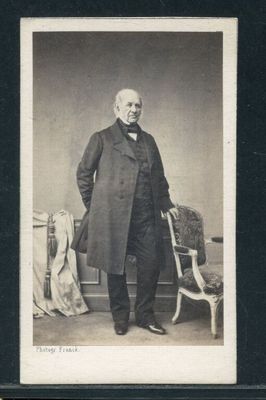 portrait d'un homme vêtu d'un long manteau, debout à côté d'une chaise