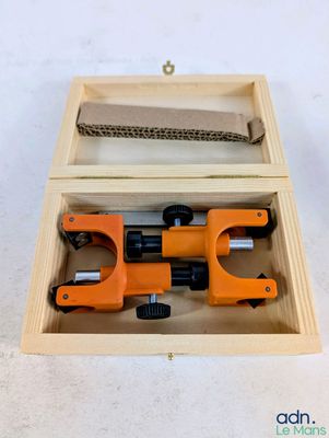 un coupe-tube orange et noir dans une boîte en bois posée sur une surface blanche