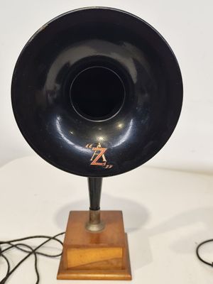 un gramophone noir posé sur un socle en bois, sur une table blanche