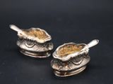 a pair of silver spoons sitting on top of a sauce dish