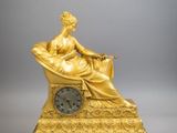 statue en or représentant une femme assise sur une chaise, avec une horloge devant elle
