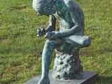 une statue représentant un homme assis sur un rocher dans l'herbe