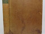 un vieux livre à la couverture marron posé sur une table blanche