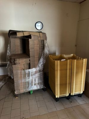 une pile de cartons dans un coin d'une pièce où est accrochée une horloge au mur