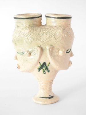 un vase blanc sur lequel est représenté un visage, avec une paire de lunettes posée dessus