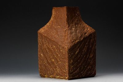 un vase marron posé sur une table sur fond noir