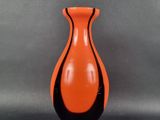 un vase orange et noir posé sur une surface grise