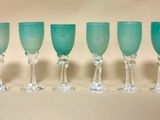 six verres à vin verts alignés en rang sur une table