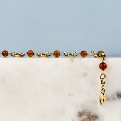 un gros plan d'un bracelet en chaîne dorée orné de perles, posé sur une surface en marbre
