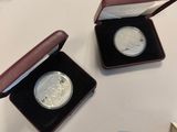 two silver coins in a case on a table with a blue box