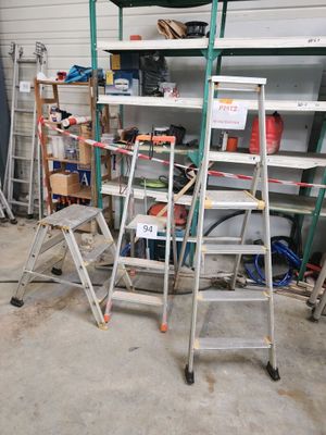 Plusieurs échelles sont empilées dans un garage, avec des outils posés dessus.