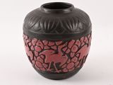 un vase noir et rouge posé sur une surface blanche