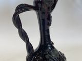 a black vase with a handle on a white table