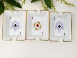 three small white and gold ashtrays with playing cards on them
