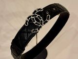 black leather bracelet with a silver chain on a stand