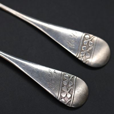 two silver spoons with designs on them on a black surface