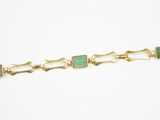 a close up of a gold bracelet with green stones on it