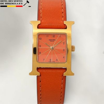 a gold watch with a red face on a tan leather strap