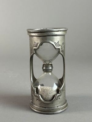 an old silver hourglass with sand in it on a gray surface