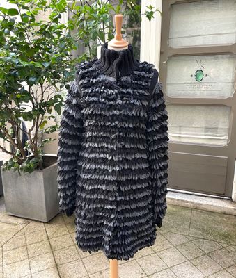black ruffled coat on a mannequin stand in front of a potted plant