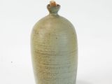a small green vase with a wooden lid on a white surface