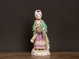 une vieille figurine représentant une femme tenant un panier, posée sur une table
